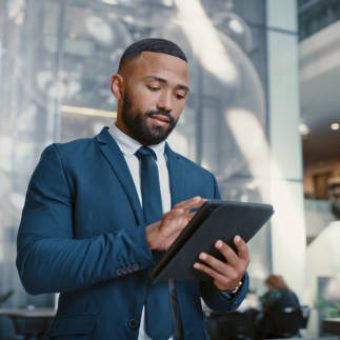 Hotel, manager and man on a digital tablet for booking, planning and accommodation management while working at front desk. Black man, concierge and hospitality by male doing online task at reception